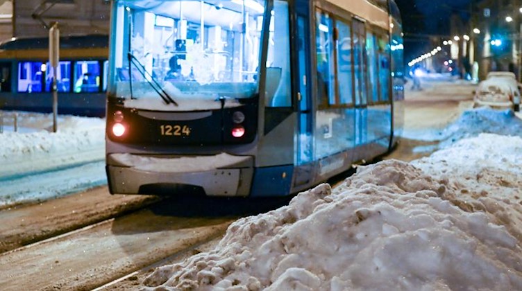 Schneehaufen liegen am frühen Morgen neben der Fahrbahn und den Straßenbahngleisen, auf denen eine Straßenbahn fährt. Foto: Hendrik Schmidt/dpa-Zentralbild/dpa/Archivbild