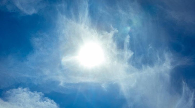Die Sonne scheint am blauen Himmel durch Wolken hindurch. Foto: Markus Scholz/dpa/Symbolbild