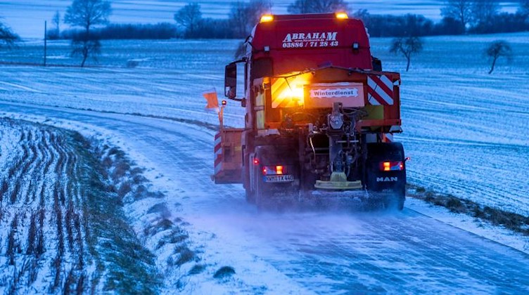 Ein Lastwagen mit einem Schneepflug streut einen Landweg. Foto: Jens Büttner/dpa-Zentralbild/dpa/Symbolbild