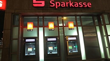 Geldautomaten sind an der Fassade einer Sparkasse beleuchtet. Foto: Oliver Berg/dpa/Archivbild