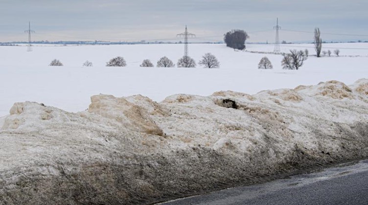 Schneehaufen liegen am Rande einer Straße die an verschneiten Feldern entlang führt. Foto: Robert Michael/dpa-Zentralbild/dpa
