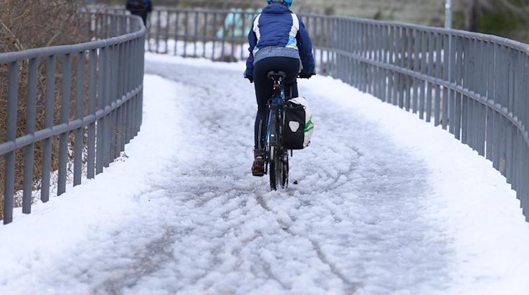 Eine Radfahrerin fährt auf einem verschneiten Radweg entlang. Foto: Sebastian Kahnert/dpa-Zentralbild/dpa/Archivbild