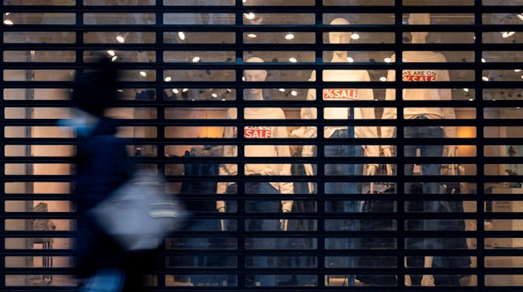 Eine Passantin geht auf einer Einkaufspassage an einem geschlossenen Bekleidungsgeschäft vorbei. Foto: Marijan Murat/dpa/Symbolbild