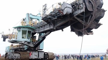 Schaulustige beobachten, wie ein 345 Tonnen schwerer Braunkohlebagger die B176 überquert. Foto: Sebastian Willnow/dpa-Zentralbild/dpa