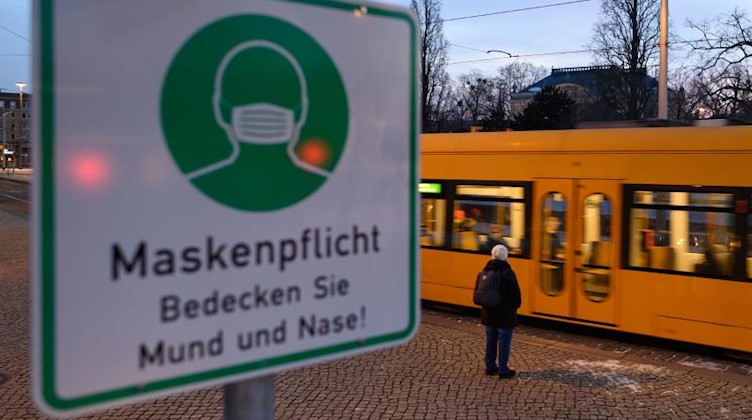 Hinter einem Maskenpflicht-Hinweis fährt auf dem Albertplatz in Dresden eine Straßenbahn entlang. Foto: Robert Michael/dpa-Zentralbild/dpa/Archivbild
