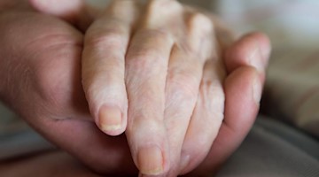 Ein Altenpfleger hält in einem Pflegeheim die Hand einer Frau. Foto: Sebastian Kahnert/zb/dpa