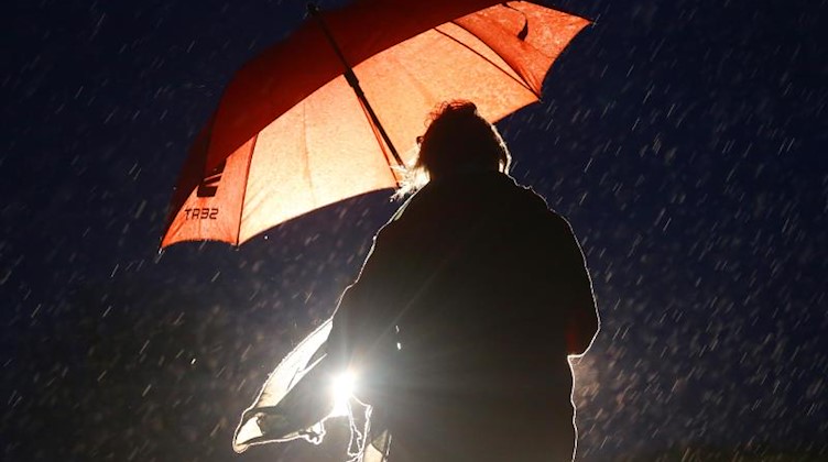 Eine Frau ist am frühen Morgen bei Regen mit Regenschirm auf dem Weg zu ihrer Arbeit. Foto: Roland Weihrauch/dpa/Archivbild