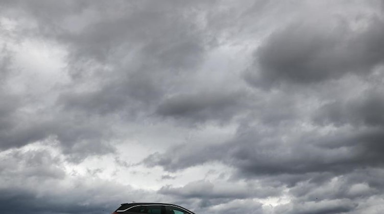 Ein Auto fährt unter einem Himmel voller dunkler Wolken. Foto: Jan Woitas/dpa-Zentralbild/dpa