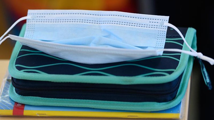 Eine medizinische Maske liegt auf einer Schulmappe in einem Klassenzimmer. Foto: Robert Michael/dpa-Zentralbild/dpa