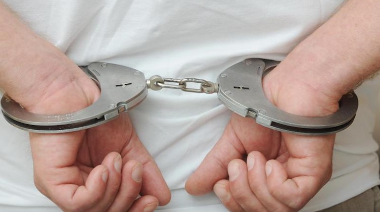 Zwei Hände sind in Polizeihandschellen gefesselt. Foto: Uli Deck/dpa/Symbolbild