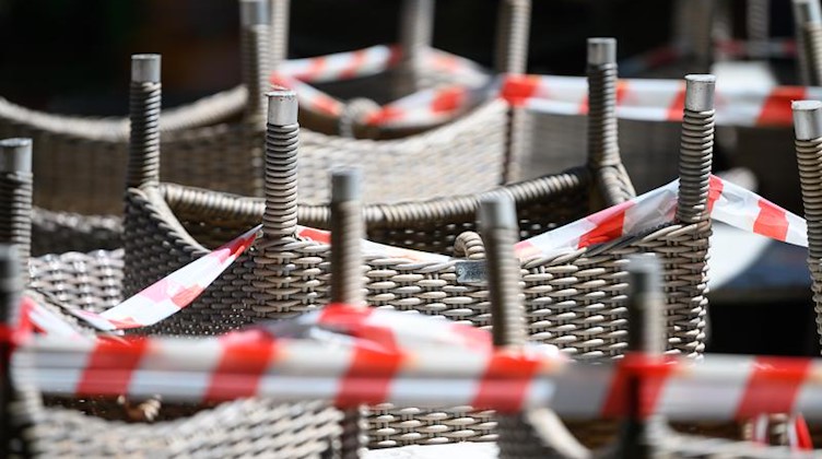 Gestapelte Stühle eines Restaurants sind mit Absperrband umgeben. Foto: Sebastian Gollnow/dpa/Symbolbild