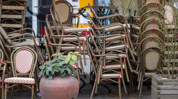 Gestapelte Stühle stehen vor einem Café. Foto: Daniel Karmann/dpa/Symbolbild