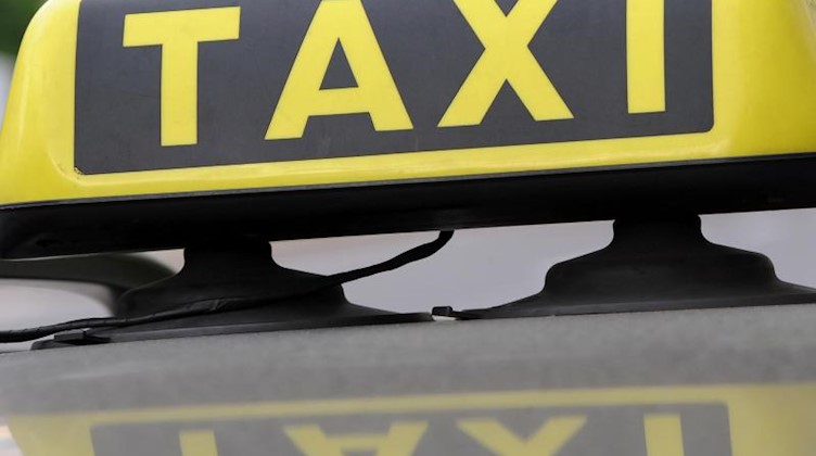 Ein Taxischild spiegelt sich in einem Autodach. Foto: Franziska Kraufmann/dpa/Symbolbild