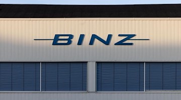 Das Logo des Sonderfahrzeughersteller Binz auf einer Werkhalle wird von der Sonne angeleuchtet. Foto: Michael Reichel/dpa-Zentralbild/dpa
