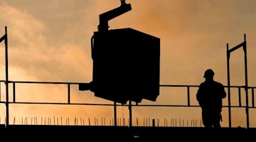 Bauarbeiter bauen bei Sonnenaufgang an einem Wohnhaus. Foto: Julian Stratenschulte/dpa/Archivbild