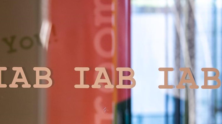 Das Logo vom Institut für Arbeitsmarkt- und Berufsforschung, IAB, steht mehrfach auf einer Glasscheibe in den Büros der Behörde. Foto: Daniel Karmann/dpa/Archivbild