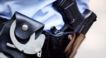 Ein Polizist mit Handschellen und Pistole am Gürtel. Foto: Oliver Berg/dpa/Archivbild