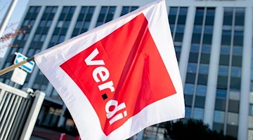 Ein Mitglied der Gewerkschaft Verdi hält eine Fahne in den Händen. Foto: Hauke-Christian Dittrich/dpa