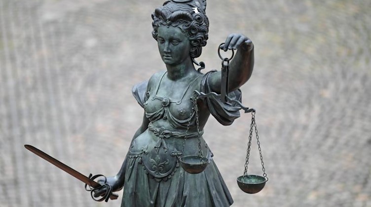 Eine Bronzefigur der Justitia steht mit Waage und Schwert in den Händen auf einem Brunnen. Foto: Arne Dedert/dpa/Symbolbild