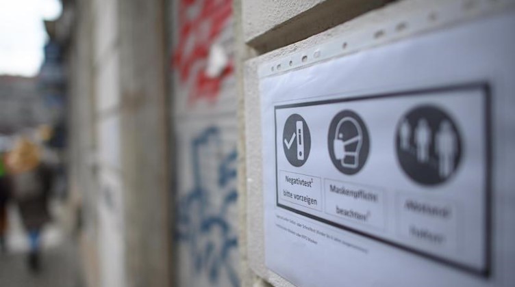Ein Zettel mit den Eintrittsbedingungen für einen Laden hängt an einer Häuserwand. Foto: Robert Michael/dpa-Zentralbild/dpa/Archivbild