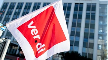 Ein Mitglied der Gewerkschaft Verdi hält an einem Tüv-Standort eine Fahne in den Händen. Foto: Hauke-Christian Dittrich/dpa