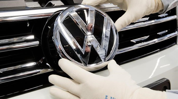 Ein Mitarbeiter montiert ein VW Logo an die Front eines VW-Wagens. Foto: Julian Stratenschulte/dpa
