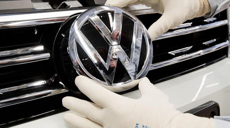 Ein Mitarbeiter montiert ein VW Logo. Foto: Julian Stratenschulte/dpa