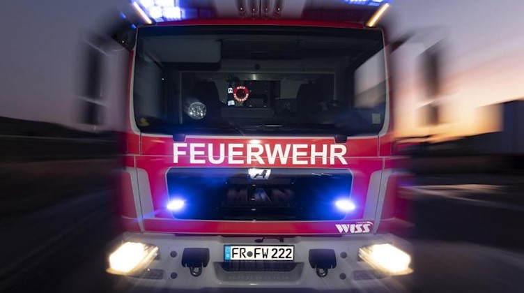 Ein Feuerwehrfahrzeug steht mit eingeschaltetem Blaulicht im Sonnenuntergang auf einer Straße. Foto: Patrick Seeger/dpa