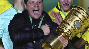 Edin Terzic (M), Dortmunds Cheftrainer, hält den Pokal im Arm. Foto: Martin Rose/POOL Getty/AP/dpa