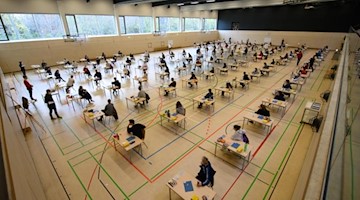 Mit weitem Abstand sitzen Schüler eines Gymnasiums zur Abiturprüfung in Deutsch an ihren Tischen in der Sporthalle. Foto: Robert Michael/dpa/Archivbild