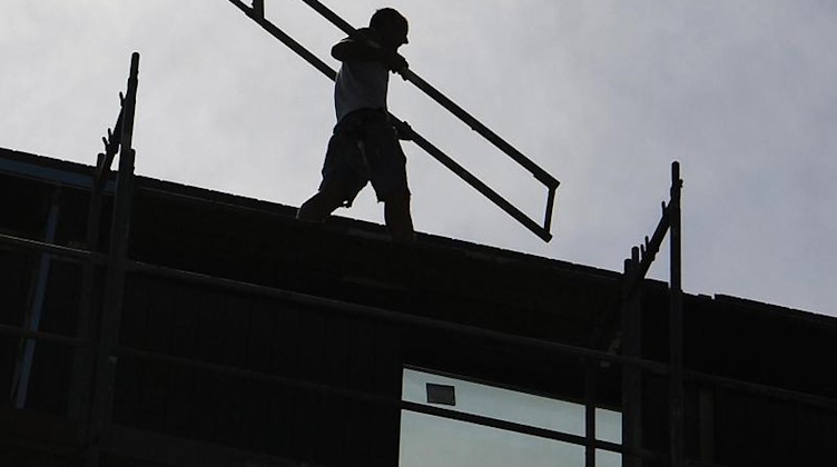Ein Arbeiter trägt auf einer Baustelle ein Teil eines Baugerüsts. Foto: Britta Pedersen/dpa-Zentralbild/dpa/Symbolbild