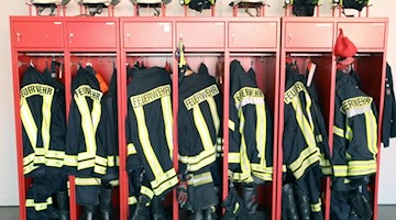 Feuerwehrjacken und -helme hängen in einem Schrank. Foto: Bernd Wüstneck/zb/dpa/Symbolbild