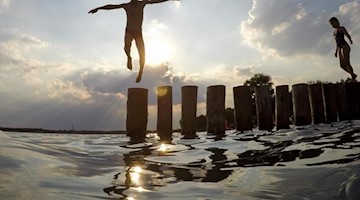 Ein Junge springt von einer Buhne in einen See. Foto: Jan Woitas/dpa-Zentralbild/dpa