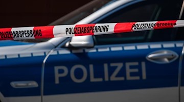Ein Polizeiauto steht hinter einem Absperrband der Polizei. Foto: Robert Michael/dpa-Zentralbild/dpa/Symbolbild