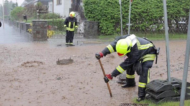 Feuerwehrleute sind im Ortsteil Geyersdorf mit Aufräumarbeiten beschäftigt. Foto: Ronny Küttner/-/dpa