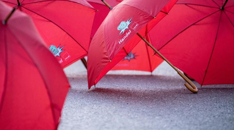 Regenschirme mit der Aufschrift «Handel ver.di» und dem Bild einer erhobenen Faust liegen bei einem Warnstreik auf dem Asphalt. Foto: Matthias Balk/dpa