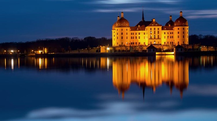Das beleuchtete Schloss Moritzburg spiegelt sich am Abend im Schlossteich. Foto: Monika Skolimowska/ZB/dpa/Archivbild