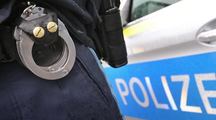 Ein Polizist mit Handschellen und einer Pistole am Gürtel steht vor einem Streifenwagen. Foto: Karl-Josef Hildenbrand/dpa