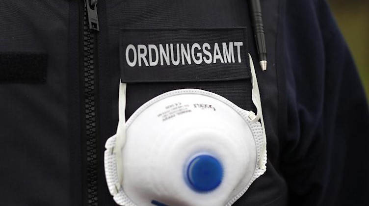 Ein Mitarbeiter des Ordnungsamts trägt einen Mundschutz an seiner Weste. Foto: Ronny Hartmann/dpa-Zentralbild/dpa/Symbolbild