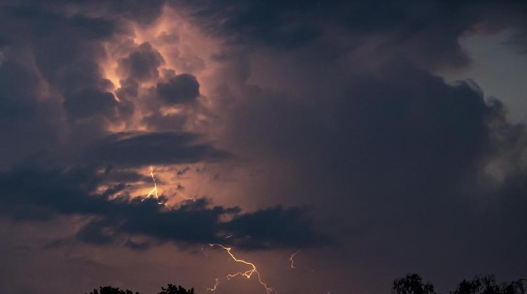 Ein Blitz hellt hinter dunklen Wolken auf. Foto: Fabian Sommer/dpa