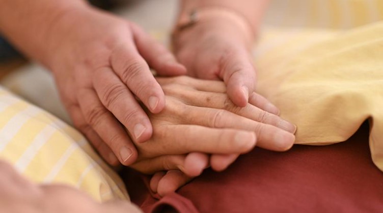Eine Hospizmitarbeiterin hält die Hand eines todkranken Menschen, der im Hospiz im Bett liegt. Foto: Felix Kästle/dpa/Archivbild
