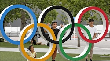 Menschen stehen stehen hinter den Olympischen Ringen in Tokio. Foto: ---/kyodo/dpa