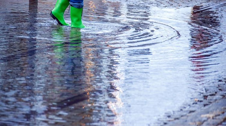 Mit Gummistiefeln geht eine Frau über eine leicht überflutete Straße. Foto: Jens Büttner/dpa-Zentralbild/dpa/Symbolbild