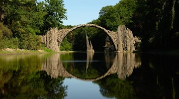 Die Rakotzbrücke bildet einen steinernen Kreis mit dem Wasser im See des Azaleen- und Rhododendren-Parks in Kromlau im Landkreis Görlitz. Foto: Robert Michael/dpa-Zentralbild/dpa