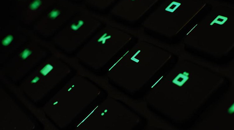 Ein Mann tippt auf einer beleuchteten Tastatur an einem Laptop. Foto: picture alliance / Nicolas Armer/dpa/Illustration