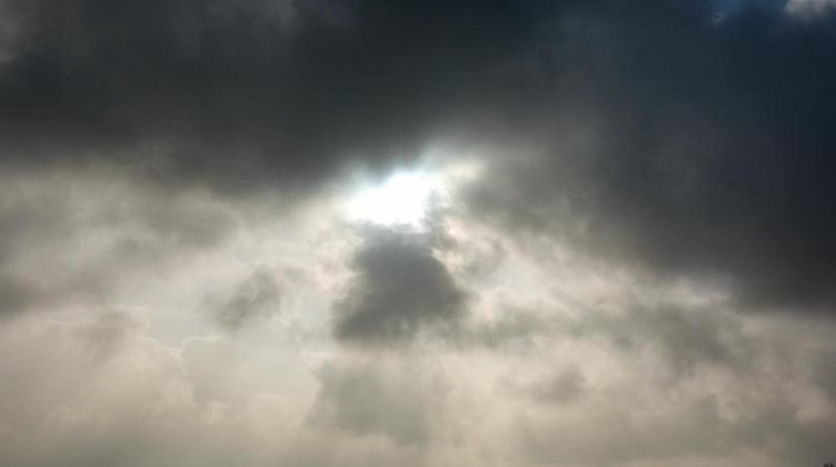 Die Sonne kommt nur kurzzeitig hinter einer dunklen Wolkendecke hervor. Foto: Jens Kalaene/dpa-Zentralbild/ZB/Symbolbild