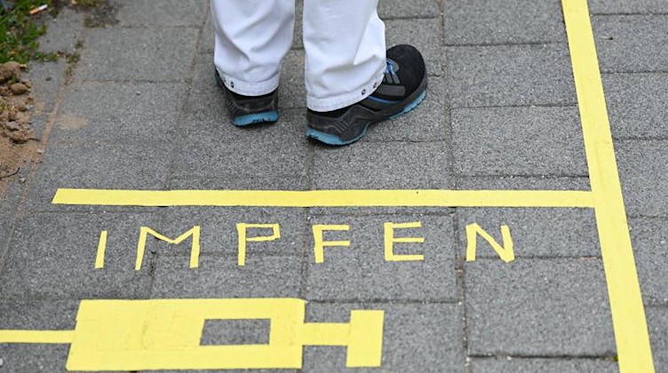 Ein Mann steht am Covid-19 Impfcenter hinter einer Bodenmarkierung mit der Aufschrift "Impfen" und einer Spritze. Foto: Arne Dedert/dpa/POOL/dpa/Symbolbild