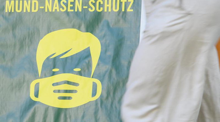 Ein Schild mit dem Hinweis auf die Maskenpflicht steht vor einem Geschäft. Foto: Robert Michael/dpa-Zentralbild/dpa