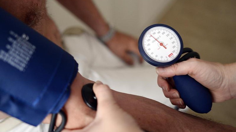Eine Medizinerin misst den Blutdruck eines Patienten. Foto: Maurizio Gambarini/dpa/Archivbild
