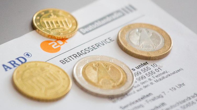 Euromünzen liegen auf einem Anschreiben zur Anmeldung für die Rundfunkgebühren, neben den Logo von ARD (l-r), ZDF und Deutschlandfunk. Foto: Fernando Gutierrez-Juarez/dpa-Zentralbild/dpa